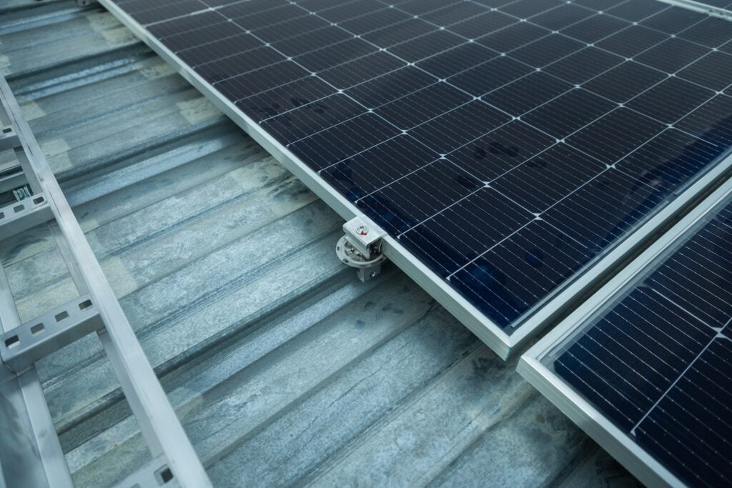 Paneles solares montados en un techo de metal corrugado, sujetos con un soporte metálico "EDGE GRAB" y "S-5!". Se ven rieles de montaje adicionales a la izquierda.